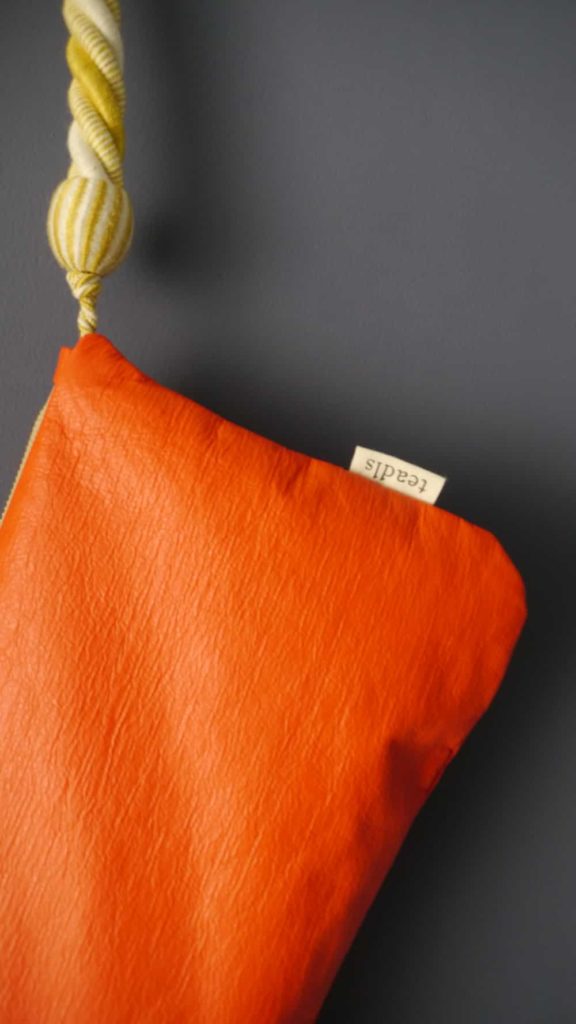 détail du sac banane tula en vinyle orange mat avec embrasse à rideau en guise d'anse