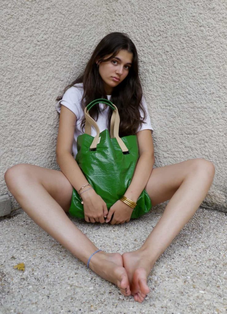 Lou la fille de la créatrice tient le cabas toumi en vinyle vert upcyclé entre ses jambes