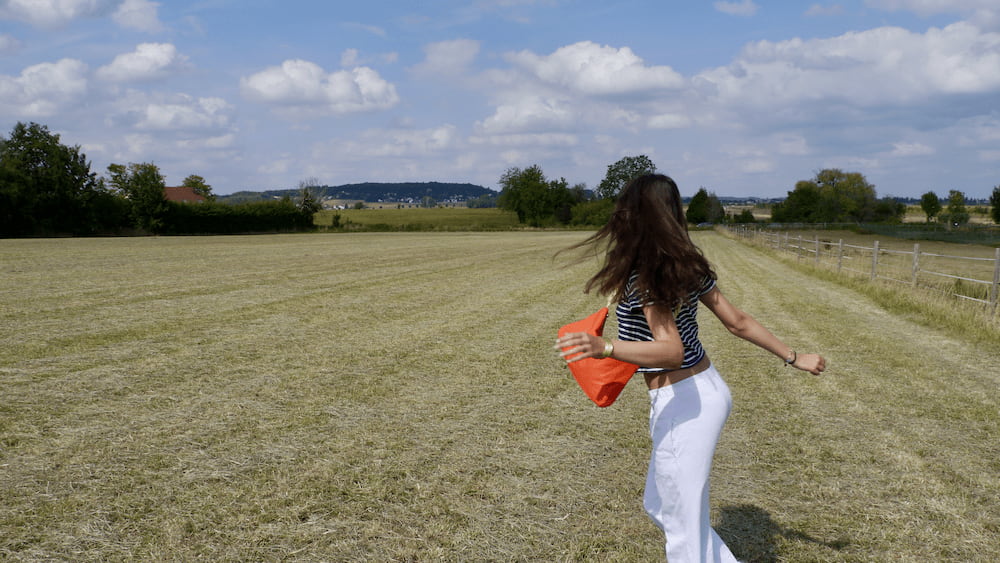 sac tula orange mat porté par lou dans un champs d'été